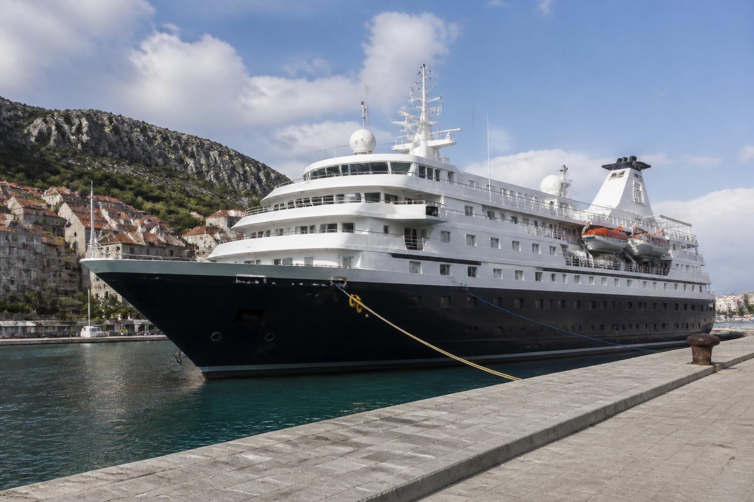 A small dark hulled expedition ship tied up alongside a stone quay in a coastal town
