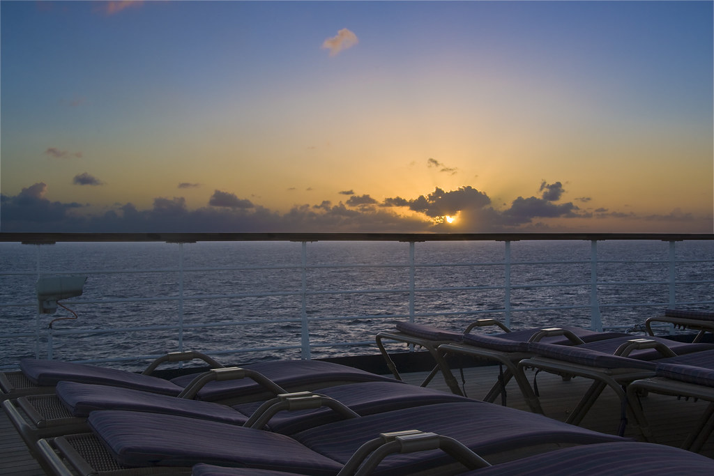 Empty loungers on a ship's deck facing the open sea at sunset